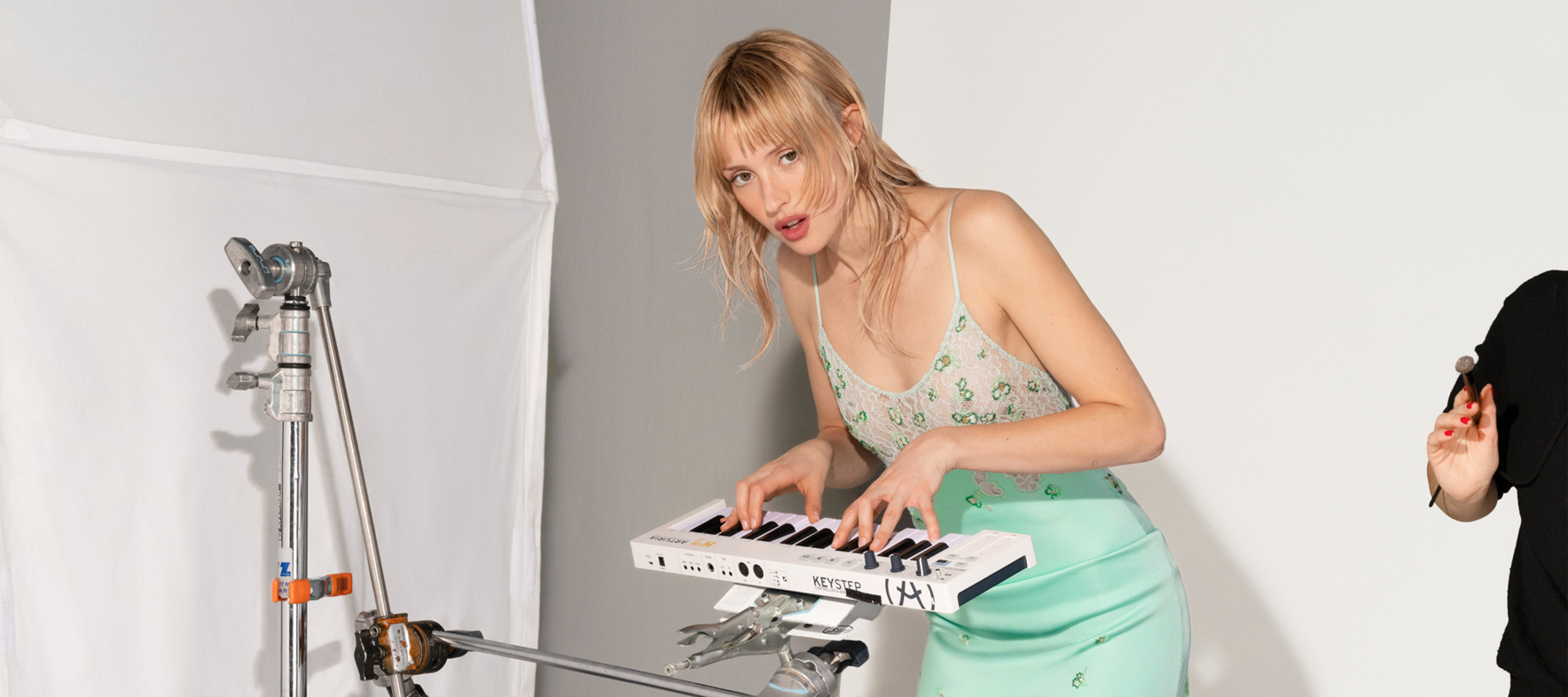 A blonde woman plays the piano while looking at the camera